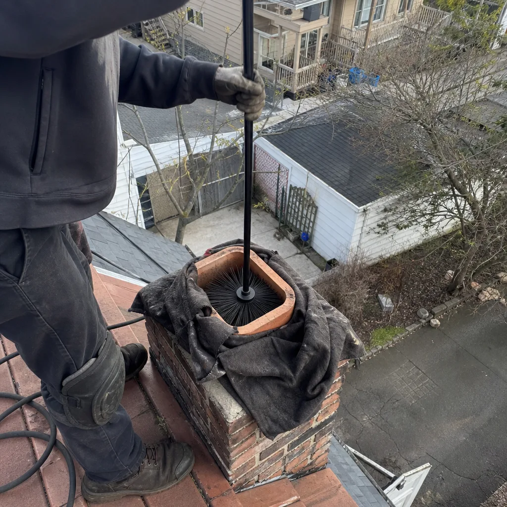 Professional chimney sweep performing chimney cleaning and maintenance on a roof.
